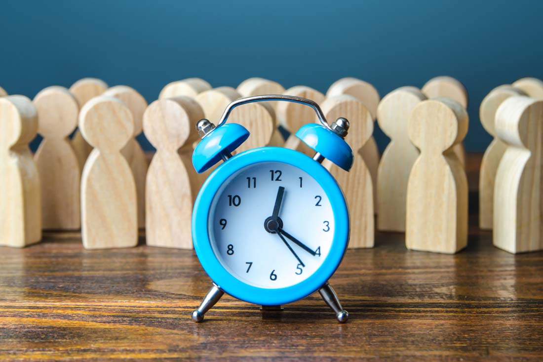 A blue clock on a desk with wooden employee blocks to symbolize employee monitoring best practices